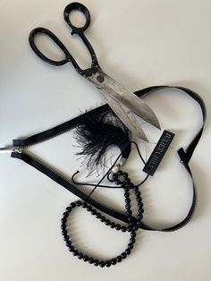 a pair of scissors and some beads on a white table with a black beaded cord