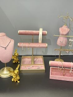 pink and gold jewelry on display in front of a gray wall with two mannequins