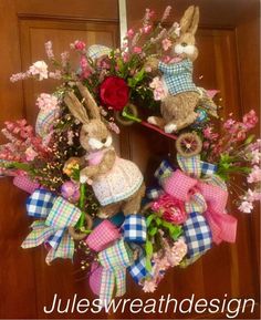 a wreath with two rabbits and flowers on it is hanging from the front door,