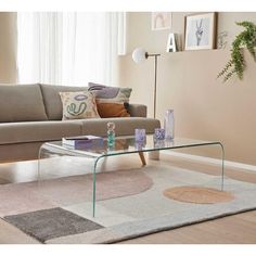 a glass coffee table sitting on top of a rug in front of a couch next to a window