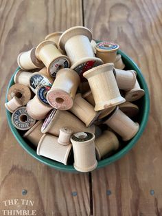 a green bowl filled with lots of spools of thread on top of a wooden table