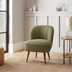 a green chair sitting in front of a window next to a table with a vase on it