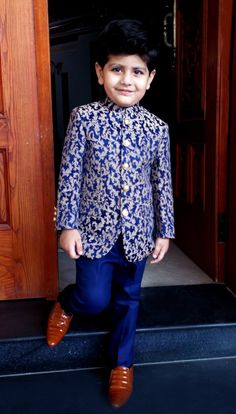 a young boy standing in front of a wooden door wearing a blue and white suit