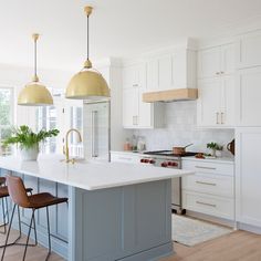 a large kitchen with white cabinets and gold pendant lights over the island, along with two bar stools