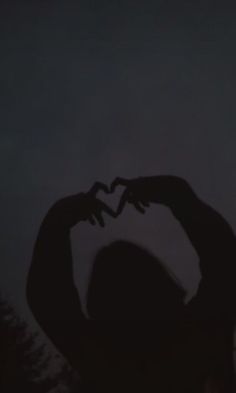 the silhouette of a woman making a heart with her hands