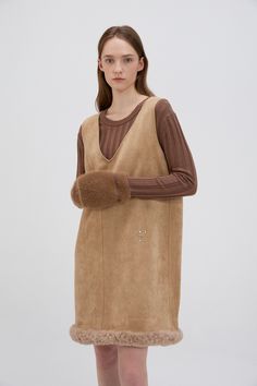 This Shearling Trimmed Suede Dress combines rustic elegance with modern design, making it a standout piece for the cooler months. Crafted from 90% suede and 10% polyurethane, the dress features a soft and luxurious texture, while the 100% shearling trim along the hem adds warmth and a tactile element to the overall look. Its relaxed A-line silhouette provides both comfort and a flattering fit, with the mini length adding a youthful, playful touch. Perfect for layering, this dress can be styled over a fitted turtleneck or paired with a cozy cardigan for a chic, autumn-ready look. The shearling trim not only enhances the dress’s warmth but also brings added texture and dimension. Complete the outfit with ankle or knee-high boots for an effortlessly stylish and versatile ensemble that transit Chic Brown Mini Dress For Winter, Chic Leather Winter Dress, Elegant Leather Winter Dresses, Elegant Winter Leather Dresses, Elegant Leather Dresses For Winter, Teddy Bear Coat, Chic Autumn, Fitted Turtleneck, Cozy Cardigan