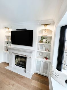 a living room with white furniture and a flat screen tv mounted on the wall above a fireplace