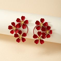 two pairs of red flower shaped earrings on top of a white piece of paper next to a wall