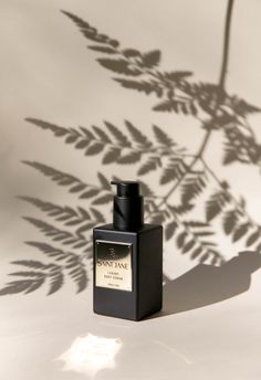 a bottle of cologne sitting on top of a white table next to a shadow of a plant