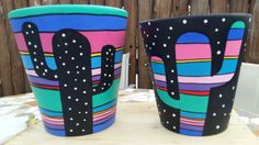 two painted cups sitting on top of a table next to each other with cactus designs