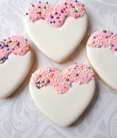 four decorated heart shaped cookies with sprinkles on white table cloth and lace