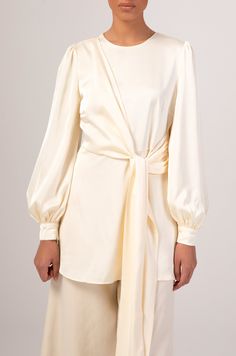 The Hala blouse features an extravagant side wrap with self fabric belt, oversized balloon sleeves and a rich satin fabric. Model is 5'7/US 02 and wears a size XS.