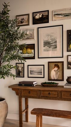 a wooden table topped with pictures and a potted plant next to a wall filled with pictures