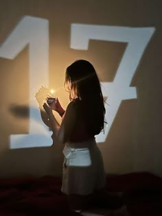 a woman holding a lit candle in her hand while standing next to a wall with numbers projected on it