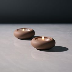 two brown candles sitting on top of a white table next to each other with one lit candle in the middle