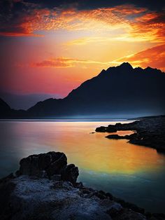 the sun is setting over water with mountains in the background