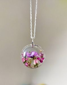 "Yorkshire forest real pressed flowers in a 22-24mm solid 925 sterling silver circle.  Hung on a solid sterling silver 925 chain stamped with certification.  This necklace symbolises spirituality, memories and represents new beginnings.  The flower is encapsulated in a crystal clear Resin which is Non-toxic, No VOCs, No fumes, No solvents, Non-flammable, Non-hazardous, No BPA.  A cute and eco friendly gift for yourself or a loved one. 🌼 So someone you love can bring spring with them wherever they go 🌼  The necklace comes in a lovely little box, hand stamped with the logo and will be posted in padded paper packaging.  🌿 Each necklace is one of a kind so may vary slightly as I have hand picked the flowers and hand made each one. 🌷🌷 Delivery:  Free Tracked and signed delivery to all coun Sterling Silver Pendant With Pressed Flowers, Delicate Sterling Silver Jewelry With Pressed Flowers, Sterling Silver Flower Jewelry With Pressed Flowers, Sterling Silver Jewelry With Pressed Flowers, Silver Necklace With Pressed Flowers Round Pendant, Silver Round Disc Jewelry With Birth Flower, Silver Jewelry With Birth Flower On Round Disc, Pink Flower-shaped Sterling Silver Necklace, Silver Flower Pendant Jewelry With Pressed Flowers