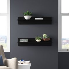 two black floating shelves with plants and books on them in front of a gray wall