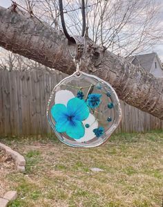 a blue flower hanging from a tree branch in front of a fence with a house behind it