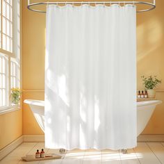 a white shower curtain sitting next to a bath tub in a bathroom under a window