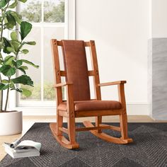 a wooden rocking chair sitting on top of a rug next to a potted plant