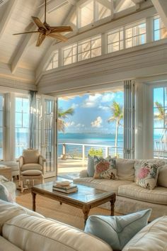 a living room filled with white furniture and large windows overlooking the ocean on a sunny day