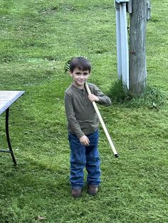 a young boy holding a baseball bat in the grass next to a table and bench