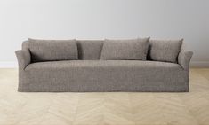 a gray couch sitting on top of a wooden floor next to a white wall in an empty room