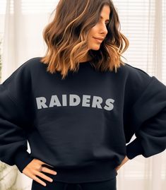 Embrace your loyalty to the Las Vegas Raiders with our bold Crewneck Sweatshirt featuring "Raiders" in striking lettering. This football sweatshirt is designed to keep you warm and stylish while you cheer on your team, whether you're at the stadium or watching from home. The classic crewneck cut makes it a versatile piece for any fan's wardrobe, perfect for game days and casual outings alike. This Raiders sweatshirt is the ideal gift for any dedicated Raiders fan. Its distinctive design and comfortable fit make it a standout choice for showing support during the football season and beyond. Whether you're buying for yourself or a fellow fan, this sweatshirt embodies the spirit of the Raiders and is sure to be a treasured addition to any fan's collection. Celebrate your team with pride in th Black Tops With Ribbed Cuffs For Game Day, Team Spirit Sweatshirt With Logo Print For Fans, Black School Spirit Sweatshirt With Crew Neck, Black Tops With Lettering For Sports Events, Team Spirit Sweatshirt With Logo Print For Game Day, Team Spirit Logo Print Sweatshirt For Game Day, Team Spirit Sweatshirt With Lettering For Fan Gear, Black Collegiate Tops With Lettering, Black Sweatshirt With Text Print For Sports Season