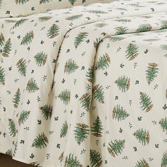 a bed with white sheets and green trees on it's coverlet is shown