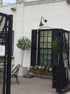 an open door on the side of a white brick building with black shutters and potted plants