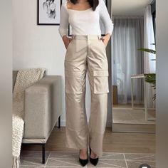 High-Waisted Pants With Side Pockets, False Back Flap Pockets, And Patch Pockets At Legs. Front Zip And Metal Hook Closure. Beige High-waisted Cargo Pants, Fitted Cargo Style Ankle-length Bottoms, Fitted Cargo Style Ankle-length Pants, Fitted Beige Pants With Side Pockets, Beige Ankle-length Cargo Pants For Work, Chic Khaki Cargo Pants For Work, Beige Cargo Pocket Ankle-length Pants, Beige High Waist Non-stretch Cargo Pants, Beige Cargo Ankle-length Pants