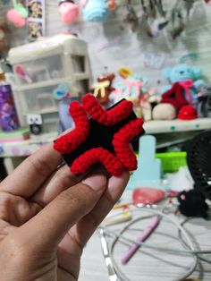 a hand holding up a small red and black star ornament in front of a cluttered room