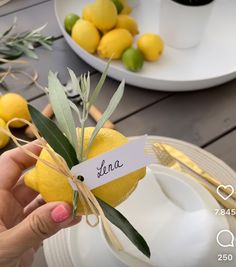 a person holding up a lemon with a name tag attached to it, next to plates and bowls