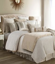 a bed with white and beige comforters in a bedroom next to a lamp on a table