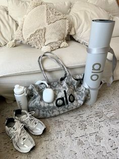 a white couch sitting next to a bag on top of a floor near shoes and sneakers