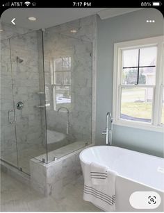 a white bathtub sitting next to a window in a bathroom with marble floors and walls