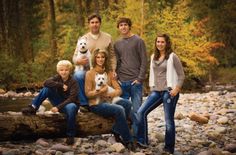 a group of people posing for a photo on a log in the water with trees behind them