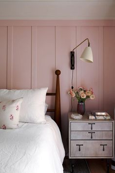 a bedroom with pink walls and white linens on the bed, bedside table next to it