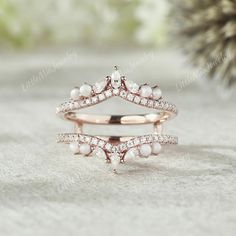 two wedding rings with diamonds and pearls on them, sitting next to a pine tree