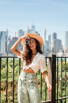 a woman wearing wide legged pants and a straw hat taking a photo with her camera