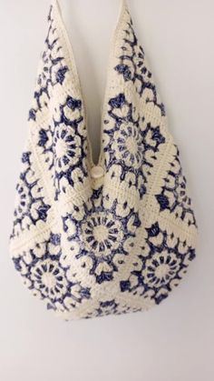 a crocheted bag hanging on the wall, with blue and white flowers in it