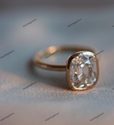 an engagement ring with a cushion cut diamond in the center on a white cloth background