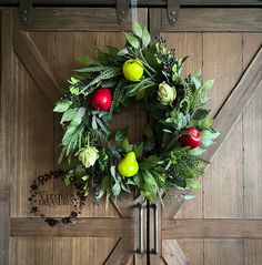 a wreath with apples, flowers and leaves hangs on the door to an old barn