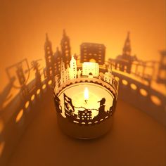 a lit candle in the shape of a cityscape with buildings and people on it