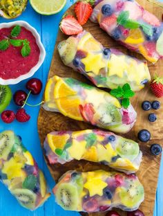 fruit pops are arranged on a cutting board with berries, kiwis, raspberry sauce and more