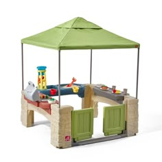 an outdoor play set with a green canopy over it and two children's toys on the table