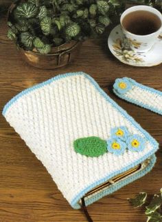 a crocheted book with flowers on it next to a cup and saucer