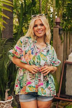 - Tropical style has arrived with this trendy top! - Unlined material with a red, pink, yellow, and green hued tropical print - A ruffled v-cut neckline with a tie detail - Short sleeves with ruffled cuffs and accent piping - A relaxed silhouette that ends in a straight hemline