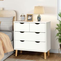 a white dresser sitting next to a bed with a lamp on it's side